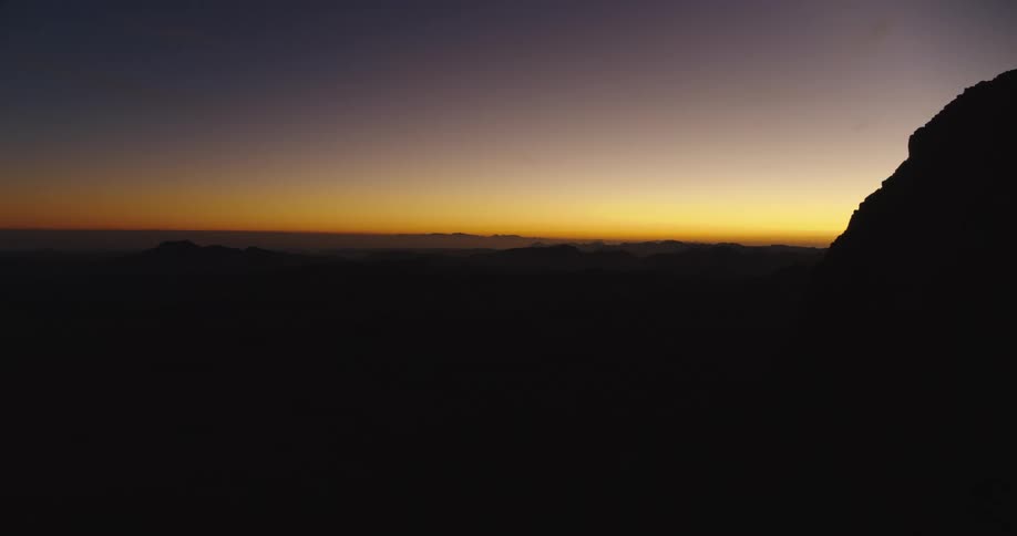 The first light of dawn paints a colorful gradient across the sky above a majestic mountain range