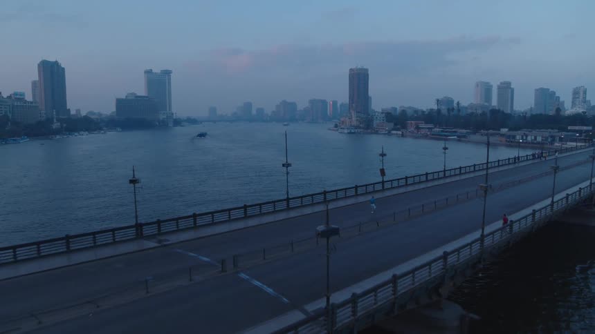 An aerial view captures a quiet morning in Cairo as a lone jogger crosses a nearly empty bridge over the Nile River at dawn