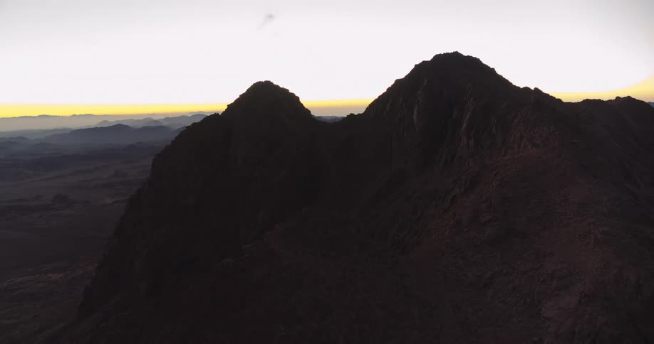 A majestic mountain peak is silhouetted against the faint glow of the rising sun on the horizon