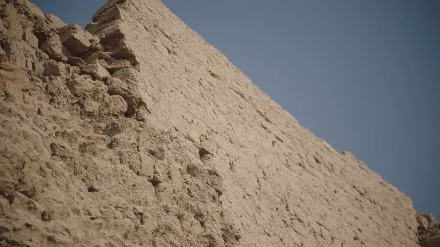 Slowly tilting up a crumbling ancient mudbrick wall against a clear blue sky