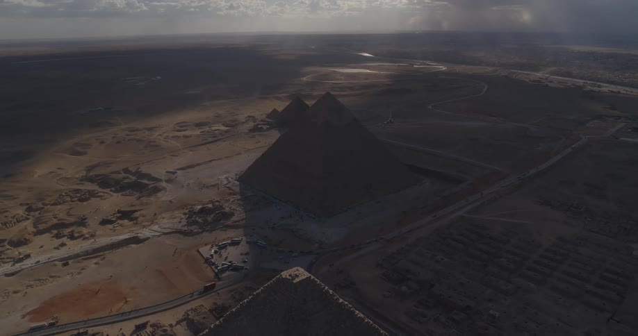 A dramatic aerial shot reveals the majestic Giza Pyramids casting long shadows across the Egyptian desert at sunset