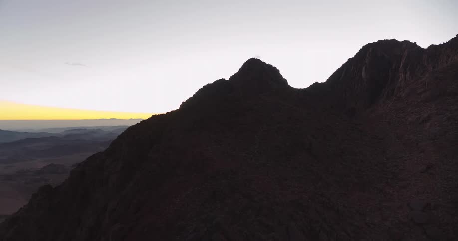 An aerial drone shot slowly approaches the dark silhouette of Mount Sinai at sunrise