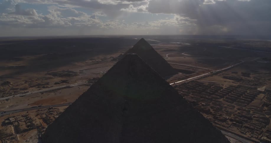 An awe-inspiring aerial ascent reveals the Great Pyramids of Giza against a vast desert landscape and a brilliant, cloudy sky