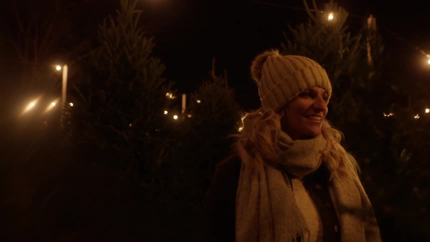 Woman smiling while looking at christmas pine tree at night