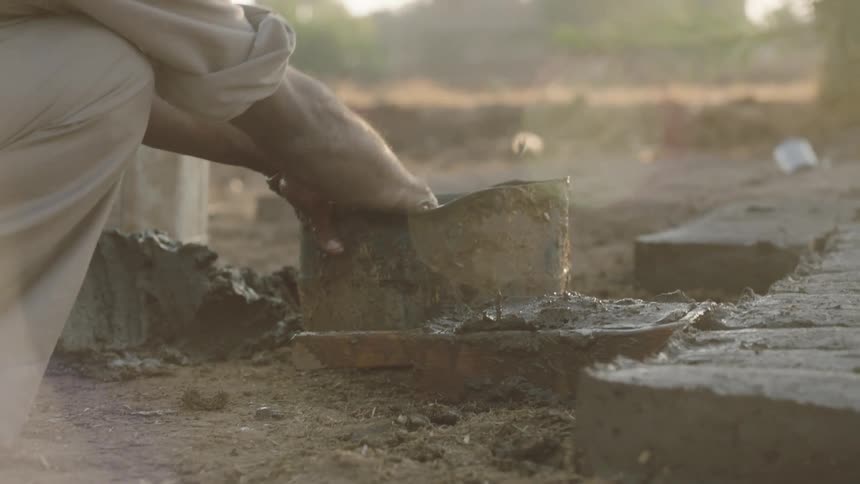 A worker's hands expertly shape wet mud into a brick using a traditional mold during a hazy golden hour