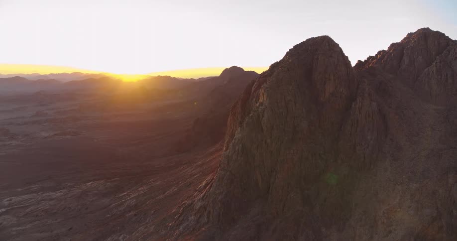 An epic aerial view shows the sun rising over a vast, rugged desert mountain range