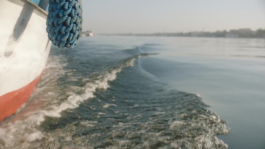 A slow-motion, low-angle view shows the gentle wake created by a boat moving through calm river water on a sunny day