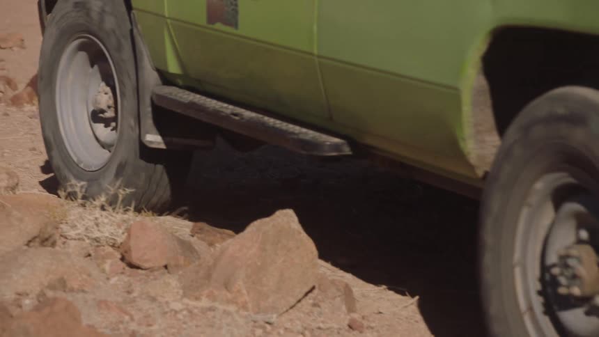 Slow motion shot of a green safari jeep driving over rocks in a dusty desert landscape