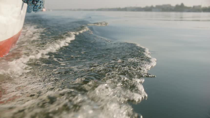 A close-up slow-motion view of a boat's wake as it glides through calm waters on a hazy morning