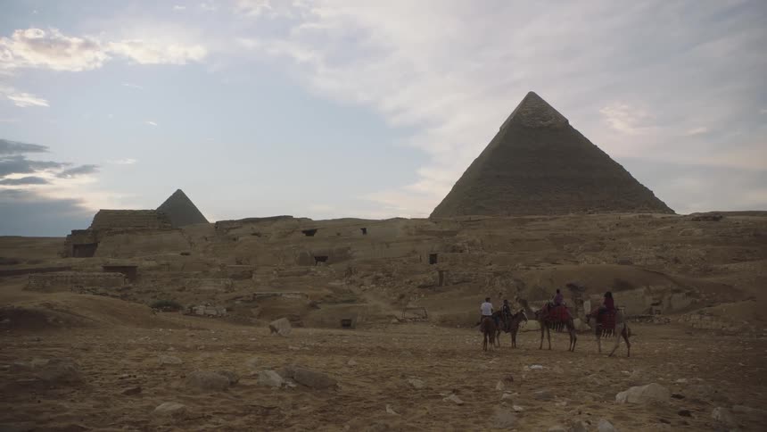 Tourists on camels pause to admire the majestic Great Pyramids of Giza in the Egyptian desert