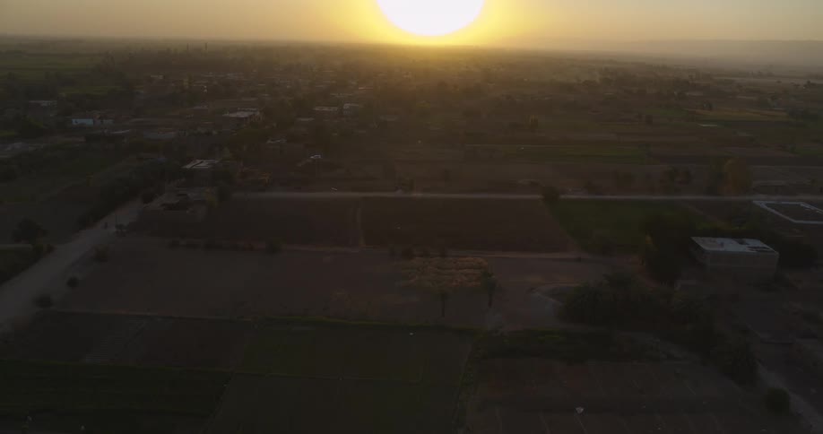 A slow drone flight over a quiet rural landscape with fields and houses during a beautiful golden hour sunset