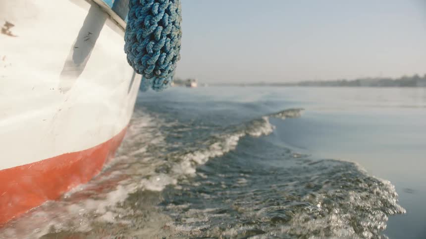 A slow-motion, low-angle view from the side of a boat shows the gentle wake it creates as it travels across a calm river