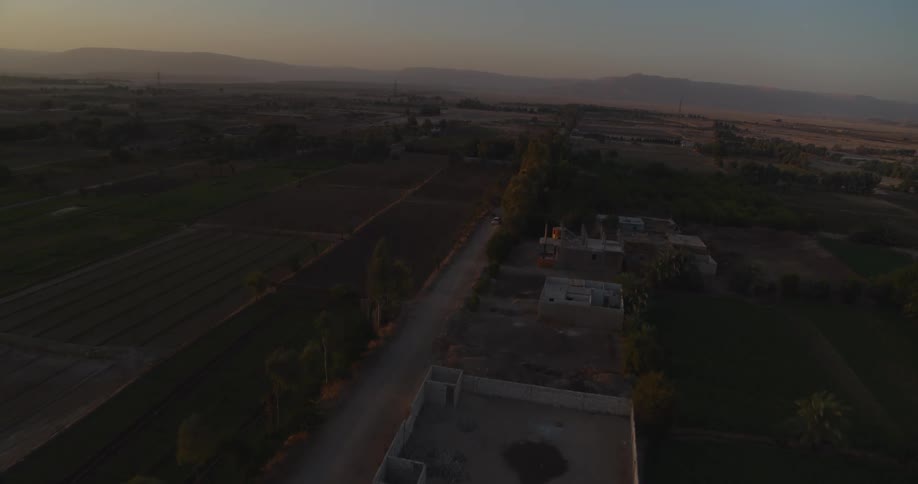 Aerial drone view flying over a rural village and farmlands at sunset