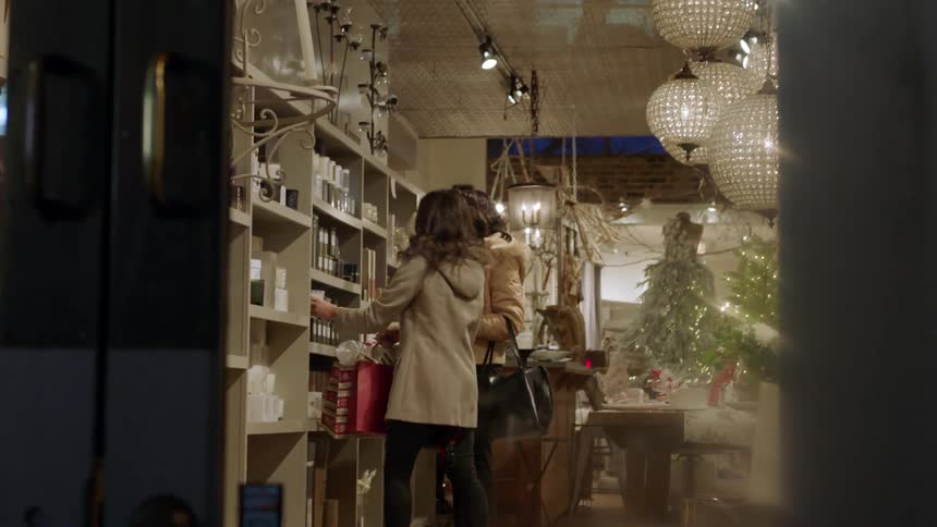 Two women pick up and smell candles while shopping