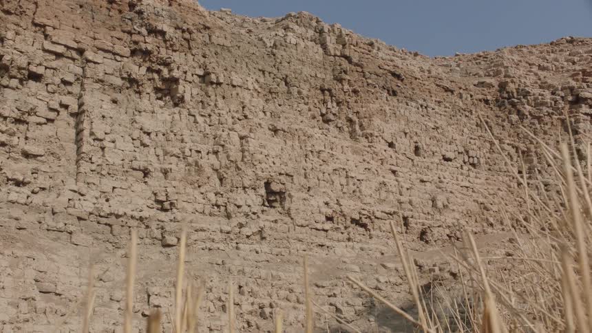 A slow pan reveals the weathered and crumbling mud brick wall of an ancient archeological site