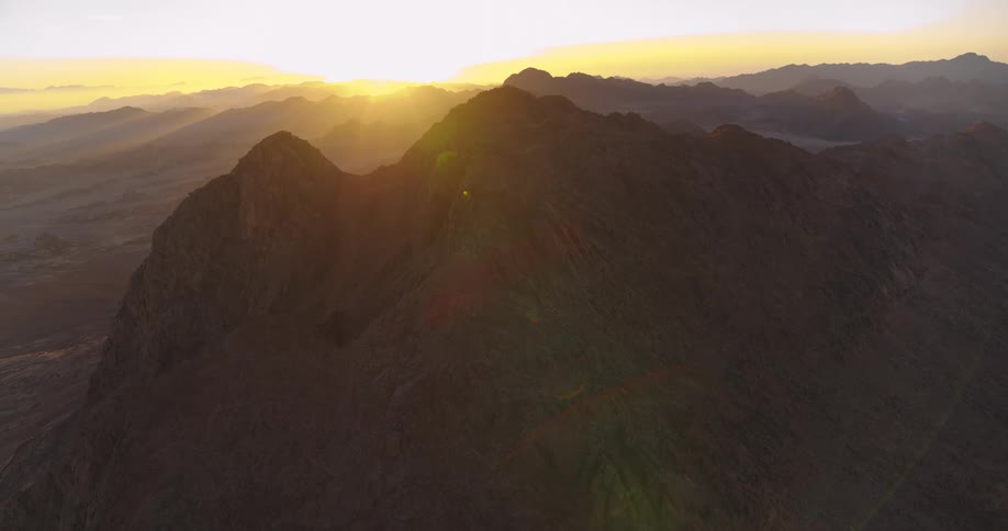 A serene aerial shot captures the golden sunrise over a vast and majestic desert mountain range
