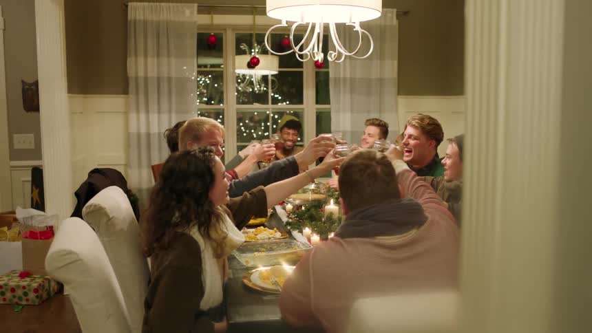 Group of people sitting at christmas dinner table cheers and take a drink