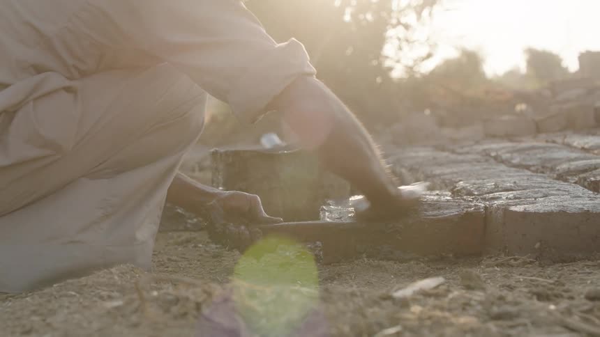 A laborer meticulously handcrafts traditional mud bricks using a simple wooden mold in the warm morning sun