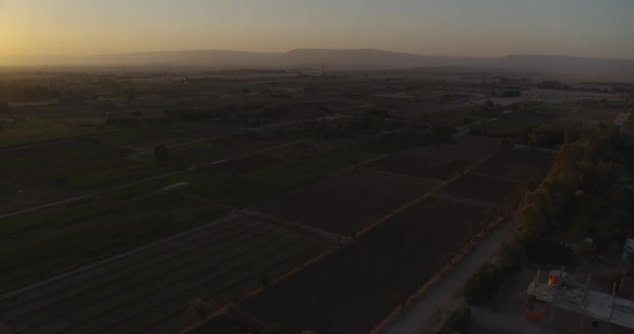 Sweeping aerial view of a vast rural landscape with agricultural fields glowing under a golden sunrise