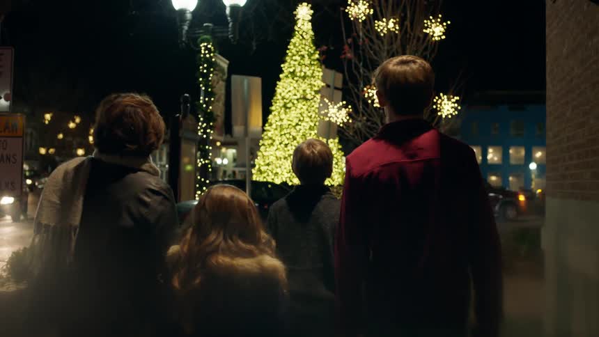 A family walks towards a glowing christmas tree in a city at night