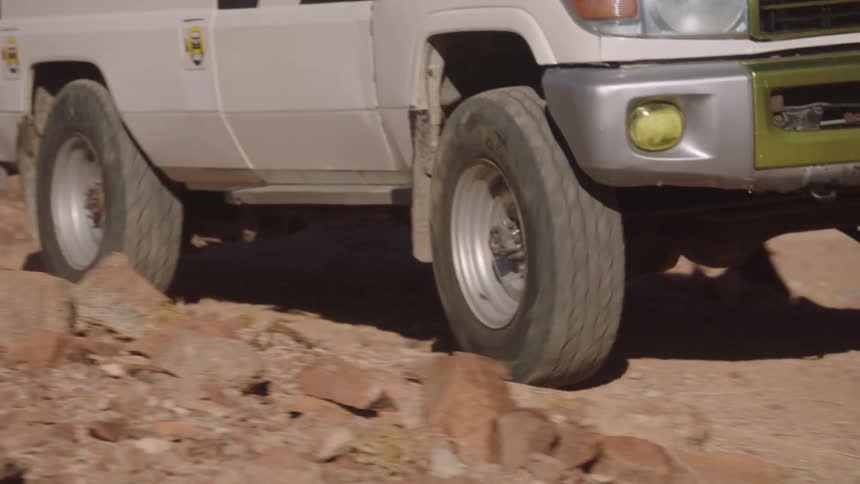 An off-road vehicle carefully navigates a rocky, unpaved desert path in slow motion