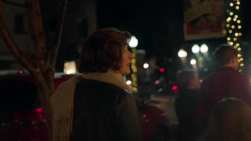 A woman and children walk down a city sidewalk that is decorated for christmas