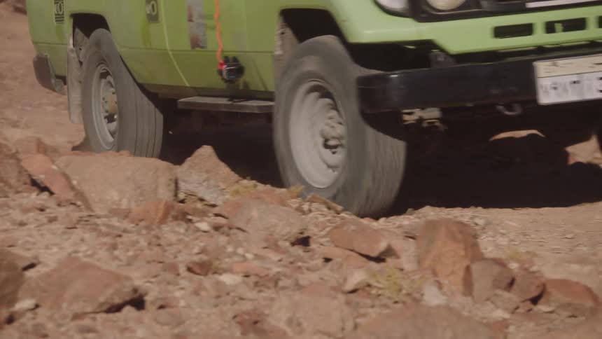 A slow-motion close-up of a rugged off-road vehicle's tires navigating a rocky desert trail
