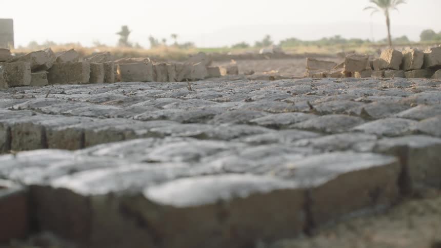 A worker makes traditional mud bricks by hand, laying them out in rows to dry in a dusty field
