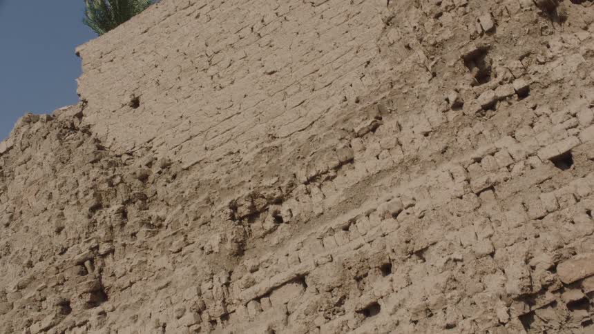 Tilting shot reveals the weathered texture of an ancient mud brick wall at an archeological site