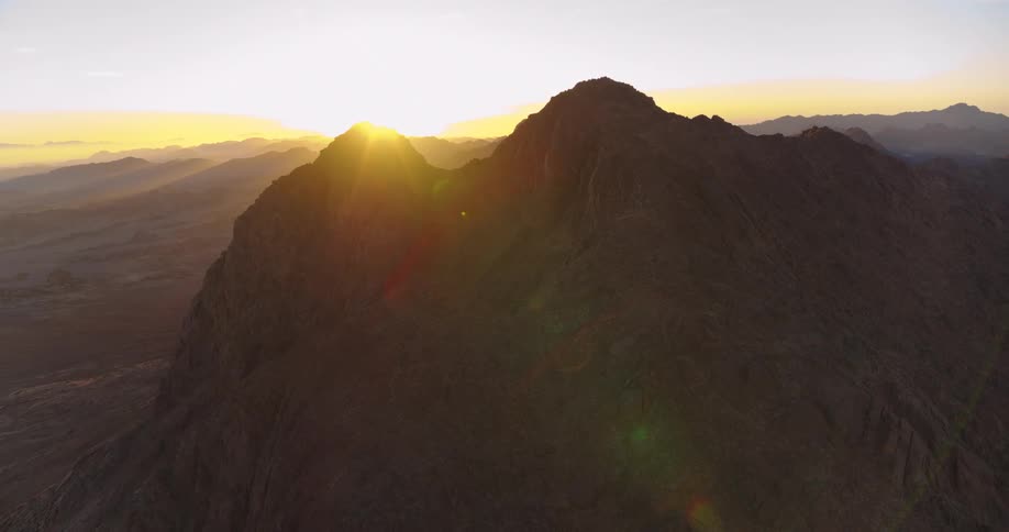 A glorious sunrise slowly crests over a majestic desert mountain range in this stunning aerial view