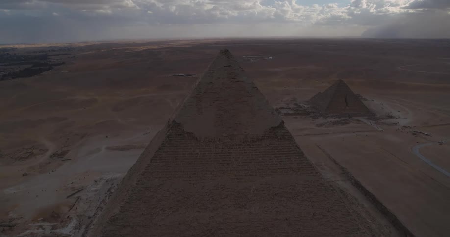 A dramatic high-angle aerial view looking down from the peak of a Giza pyramid over the vast desert landscape