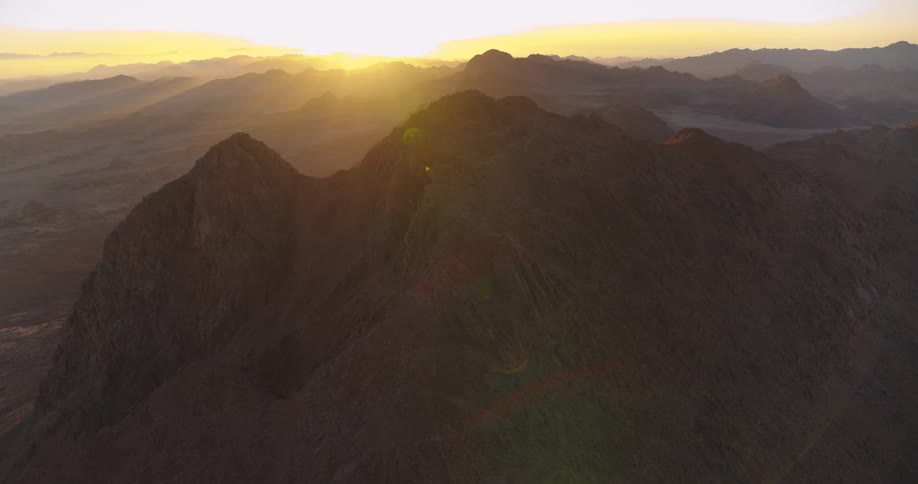 A majestic static aerial view of a desert mountain range basks in the golden glow of a stunning sunrise