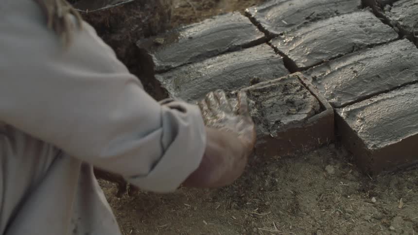Slow motion footage shows a craftsman carefully making traditional mud and straw bricks by hand
