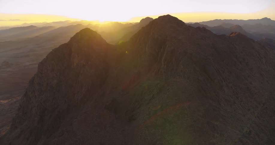 An epic aerial shot reveals the sun rising over the majestic and rugged peaks of a desert mountain range