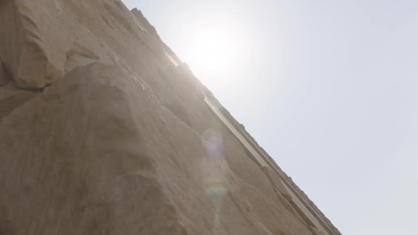 The sun slowly reveals itself from behind the massive stone blocks of the Great Pyramid of Giza with a bright lens flare