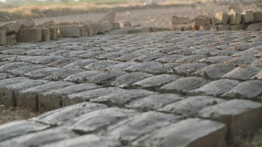 A rack focus shot reveals hundreds of handmade wet mud bricks laid out in neat rows to dry and harden in the sun