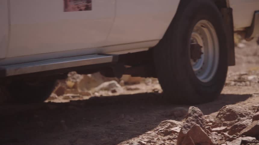 A rugged white 4x4 vehicle slowly navigates a rocky and dusty desert trail in slow motion