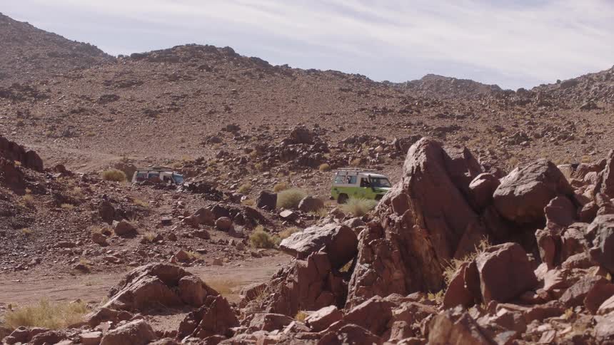 A convoy of off-road vehicles makes its way through a rugged, rocky mountain pass in the desert