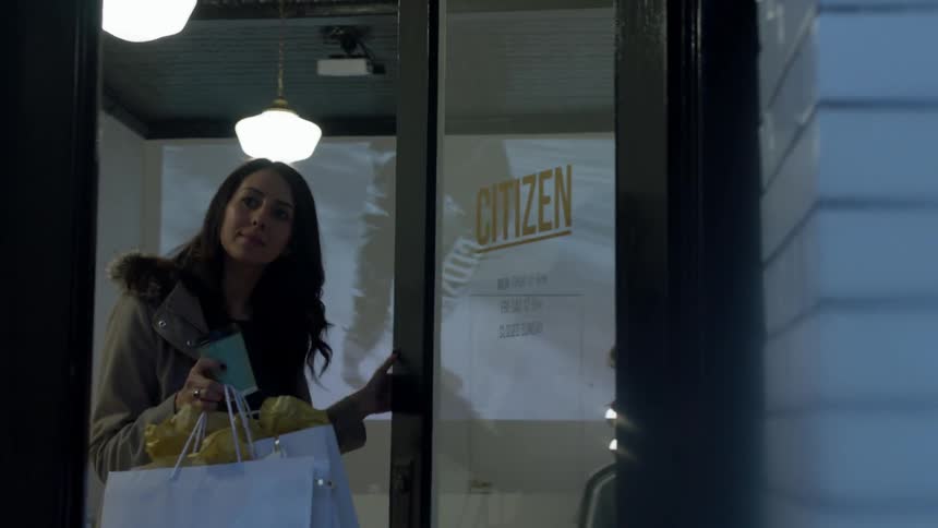 A woman carrying bags walks out of a shop door