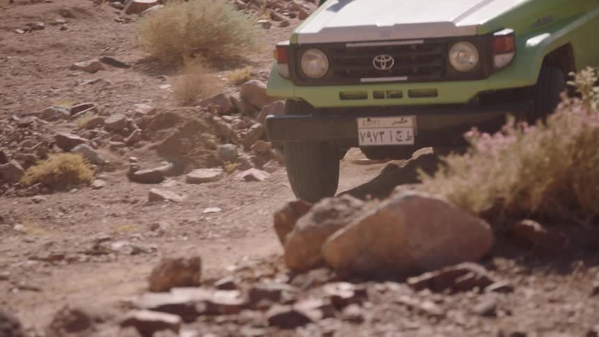 Slow motion close-up of a lime green 4x4 tour vehicle carefully maneuvering over a rocky desert trail