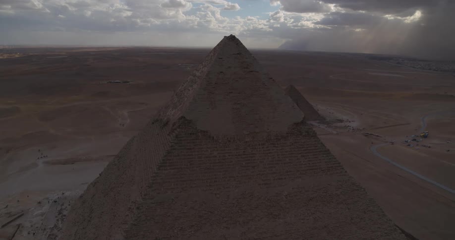 An epic aerial shot reveals the Great Pyramid of Giza in the Egyptian desert, with dramatic clouds and sunbeams in the sky