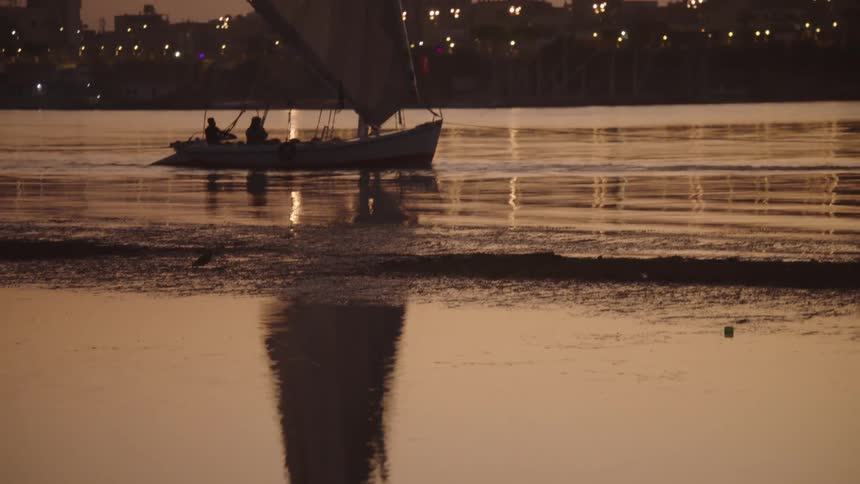 Revealing a traditional felucca sailboat on the Nile River at sunset with a slow upward tilt from its reflection