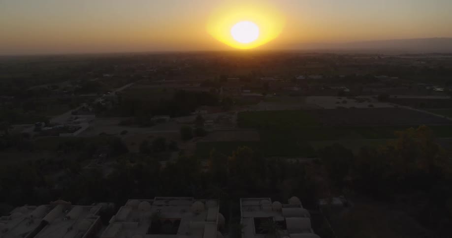 A stunning aerial shot pulls back to reveal a rural village with traditional architecture basking in the warm glow of a setting sun
