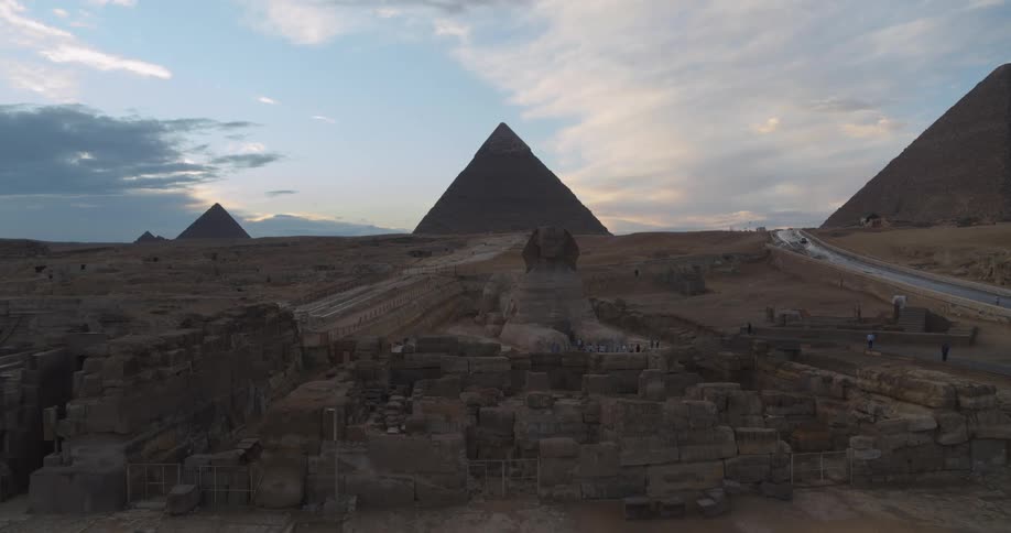 An aerial view slowly approaches the Great Sphinx of Giza at twilight, with the magnificent pyramids standing in the background
