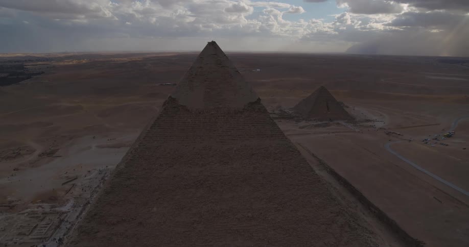 A majestic static aerial view of the Great Pyramids of Giza standing tall in the vast Egyptian desert under a cloudy sky