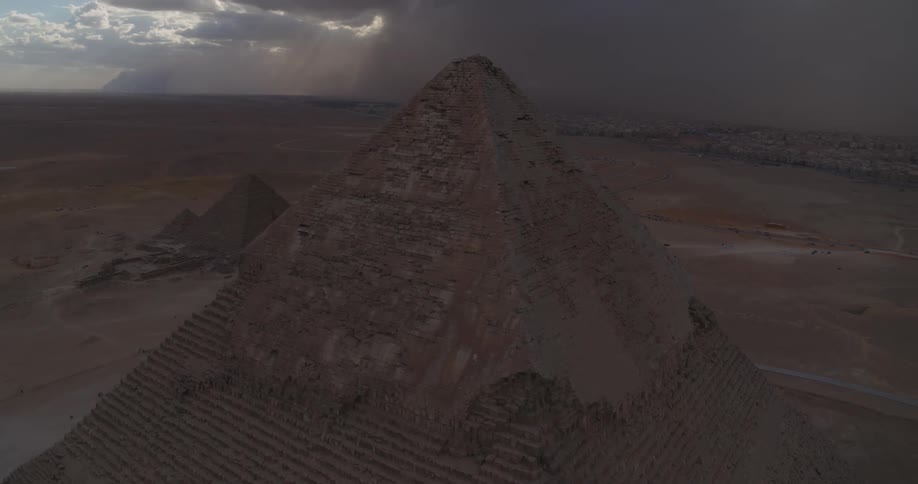 Dramatic aerial shot ascends over the Great Pyramid of Giza, revealing the ancient complex under stormy skies with divine sunbeams