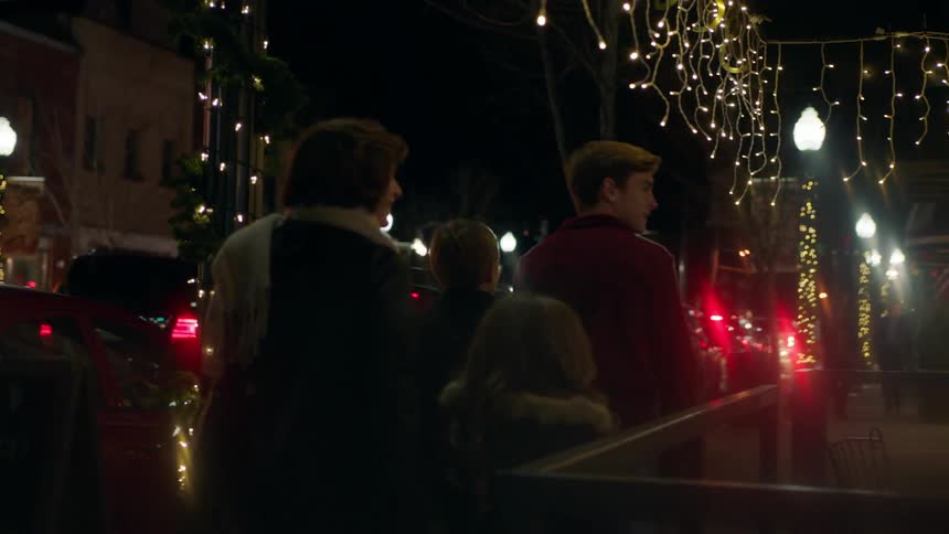 A woman and children walk past shops decorated with christmas lights
