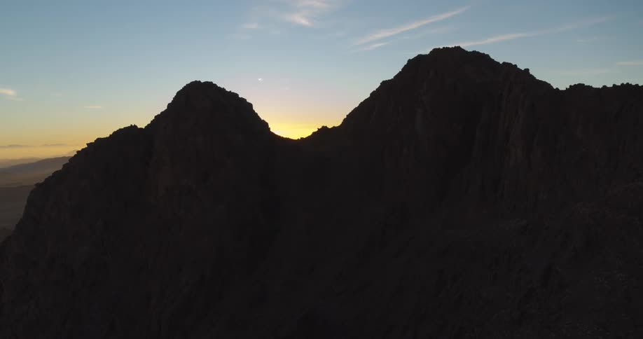 An epic sunrise crests the peak of a mountain, creating a stunning starburst lens flare against the silhouetted range