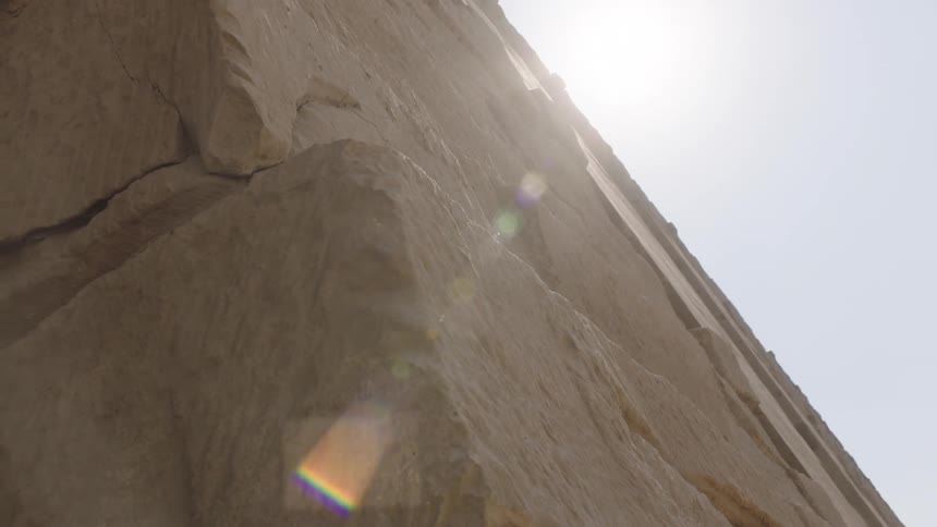 Dramatic low angle shot pulling back from the massive stone blocks of an ancient pyramid as the sun flares over the edge