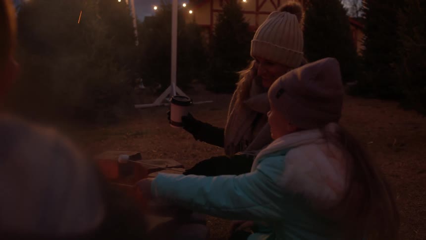 Family sitting around fire outside at night roasting marshmallows